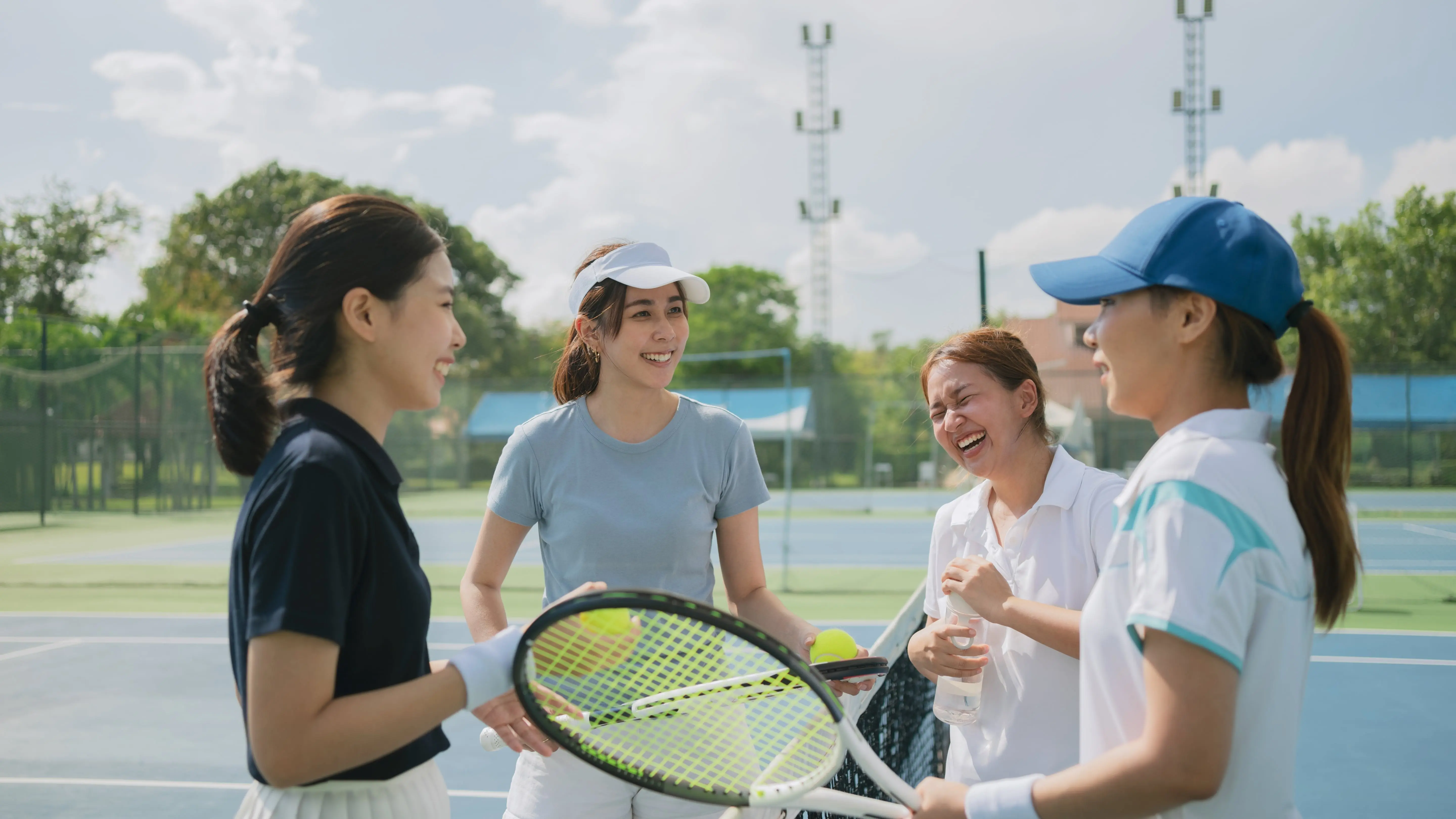 Happy asian young friendship talking and resting after match on the outdoor tennis court on a bright sunny day.