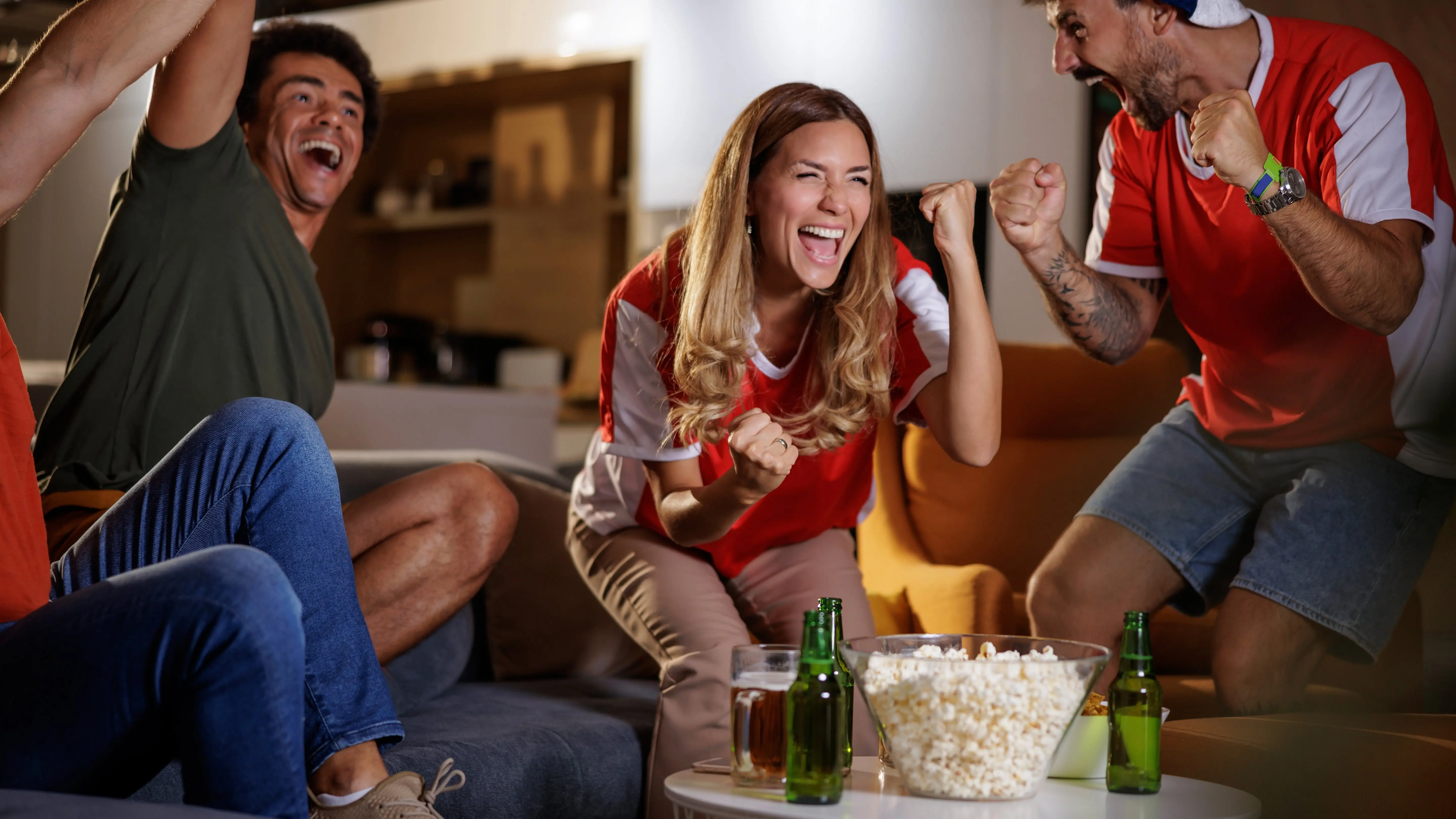 Group of young people watching and celebrating football match on television.