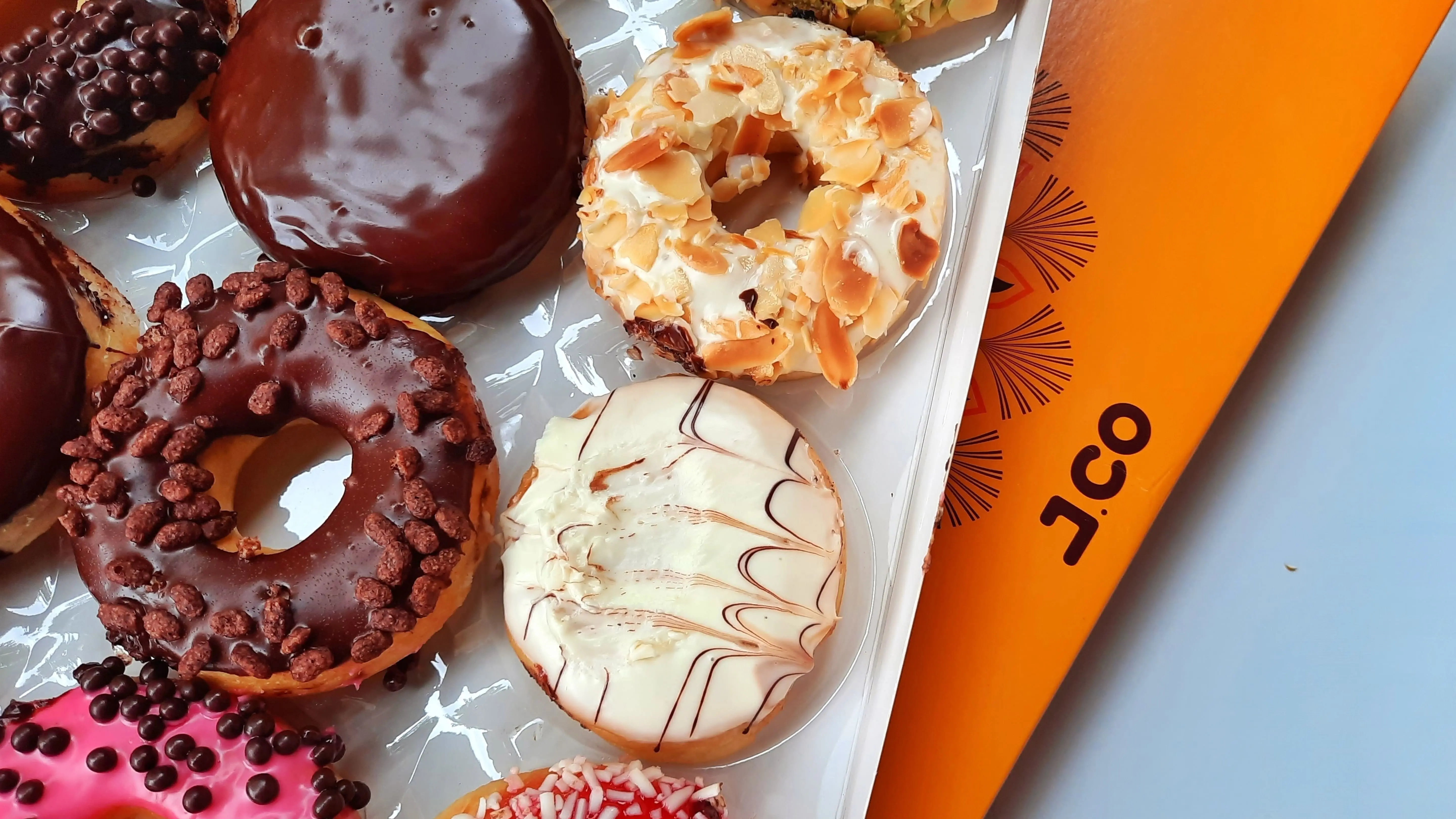 Various variants of donuts with toppings in paper box Jco donuts packaging box.