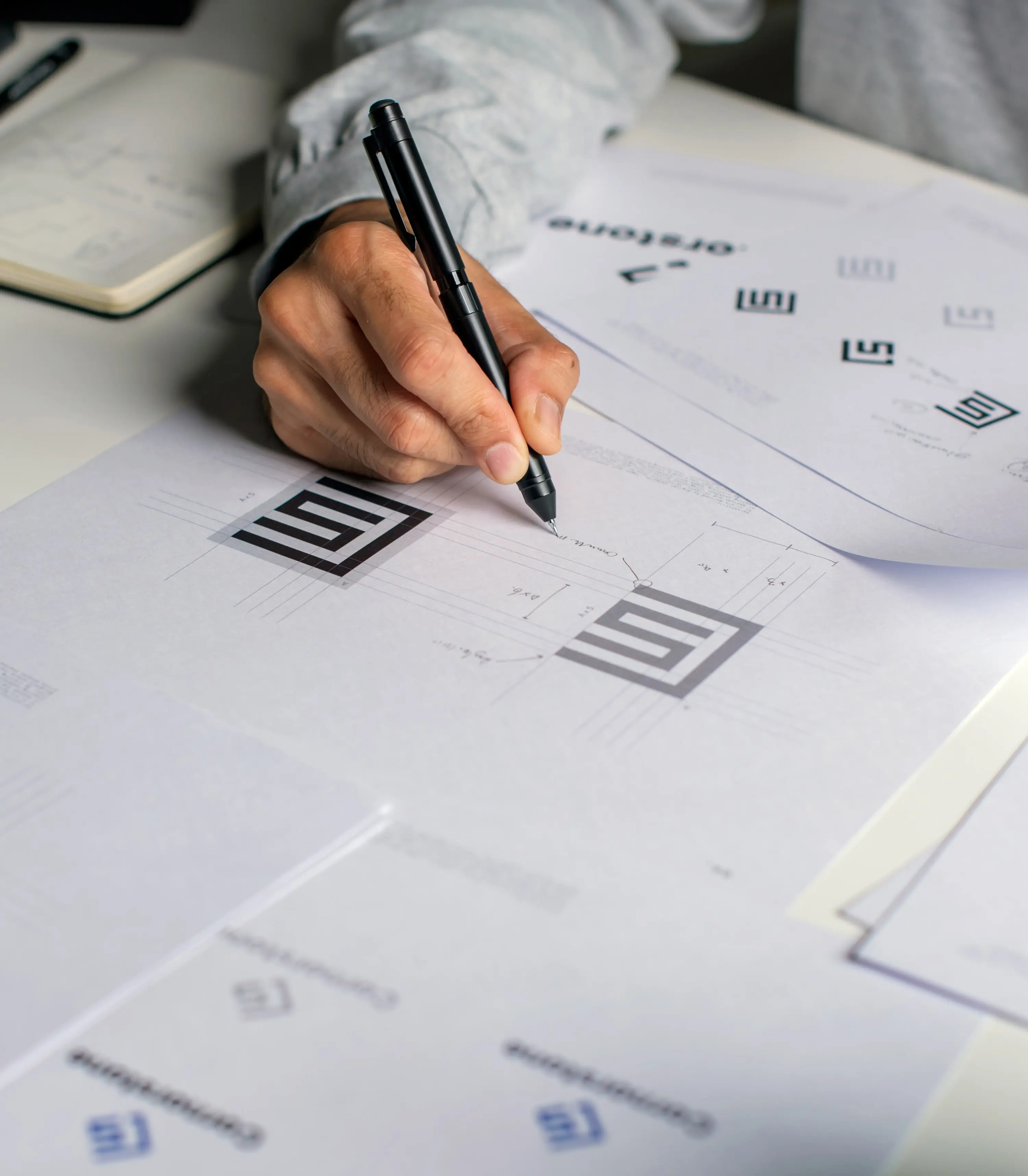 Graphic designer making notes on logo designs, using computers, designing logos, and showcasing the corporate identity and logo design process.