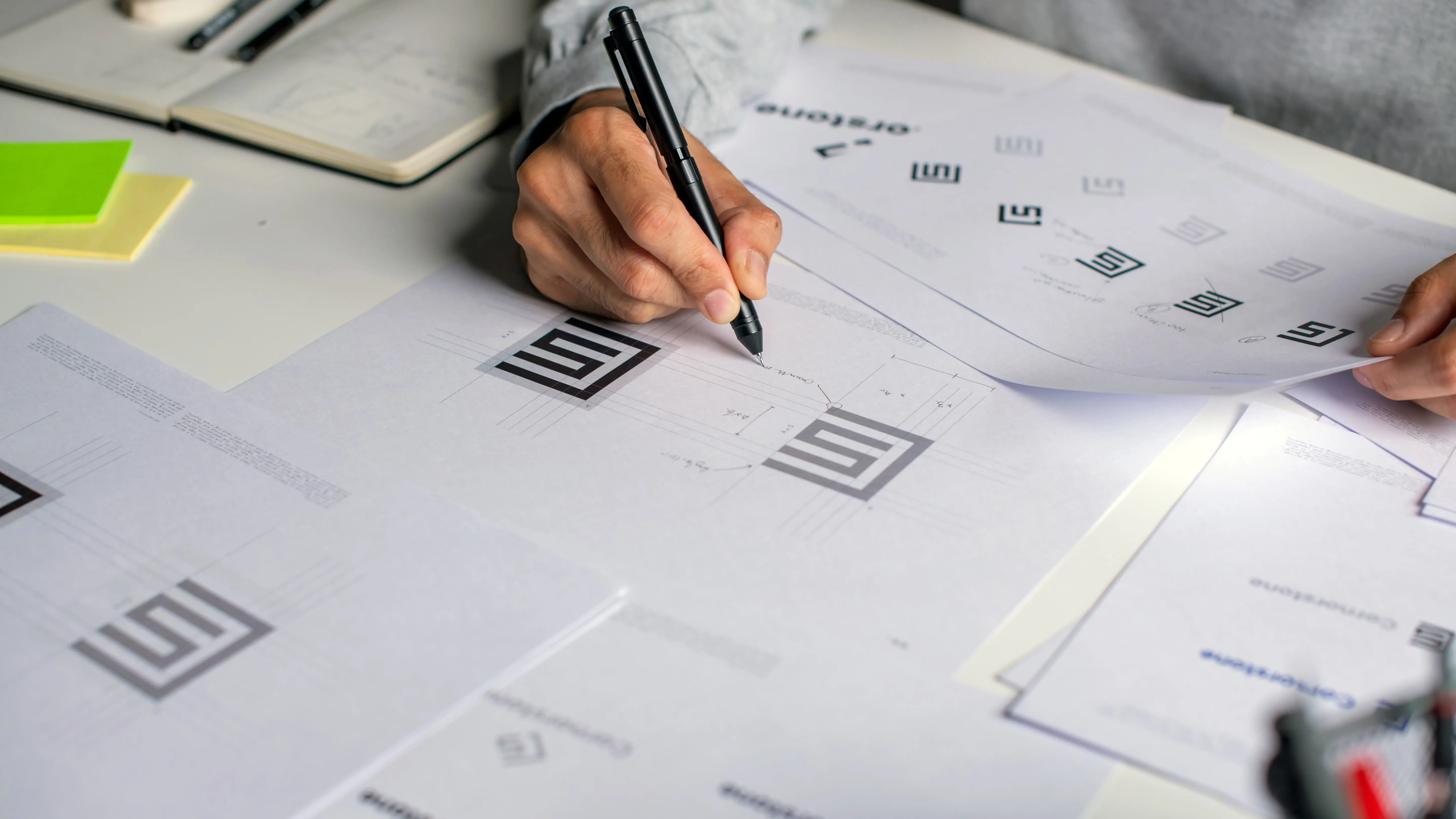 Graphic designer making notes on logo designs, using computers, designing logos, and showcasing the corporate identity and logo design process.